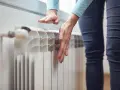 Dłonie sprawdzają temperaturę grzejnika, zastanawiając się, dlaczego grzejnik jest zimny na dole.