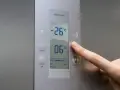 Palec naciska przycisk na panelu lodówki no frost. Wyświetlacz pokazuje -26°C i 06°C.