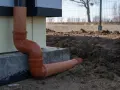 Pomarańczowe rury do odprowadzenia wody z rynien, prowadzące od budynku wprost do ziemi.