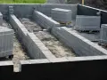 Fundament budowy z bloczków betonowych, przygotowany pod izolację przeciwwilgociową. Materiały budowlane czekają na użycie.