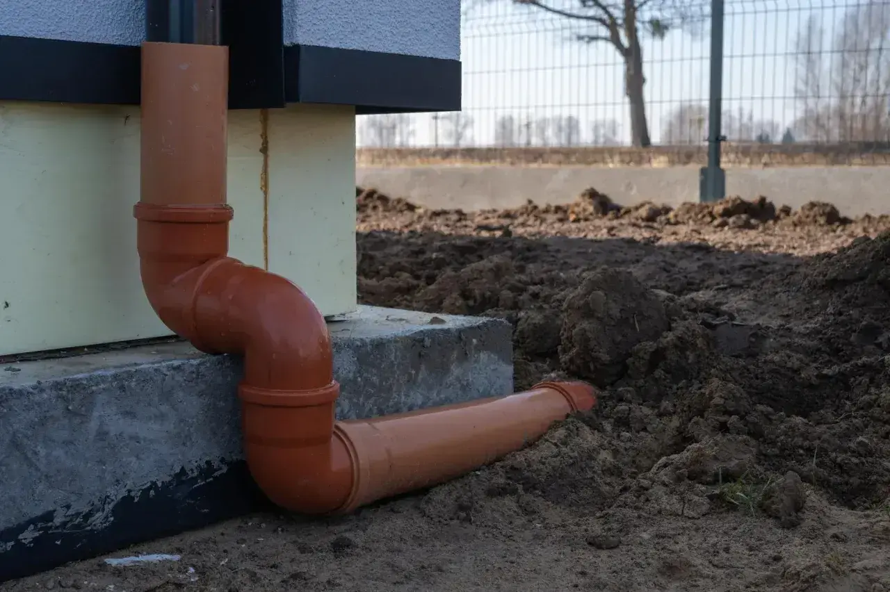 Pomarańczowe rury do odprowadzenia wody z rynien, prowadzące od budynku wprost do ziemi.