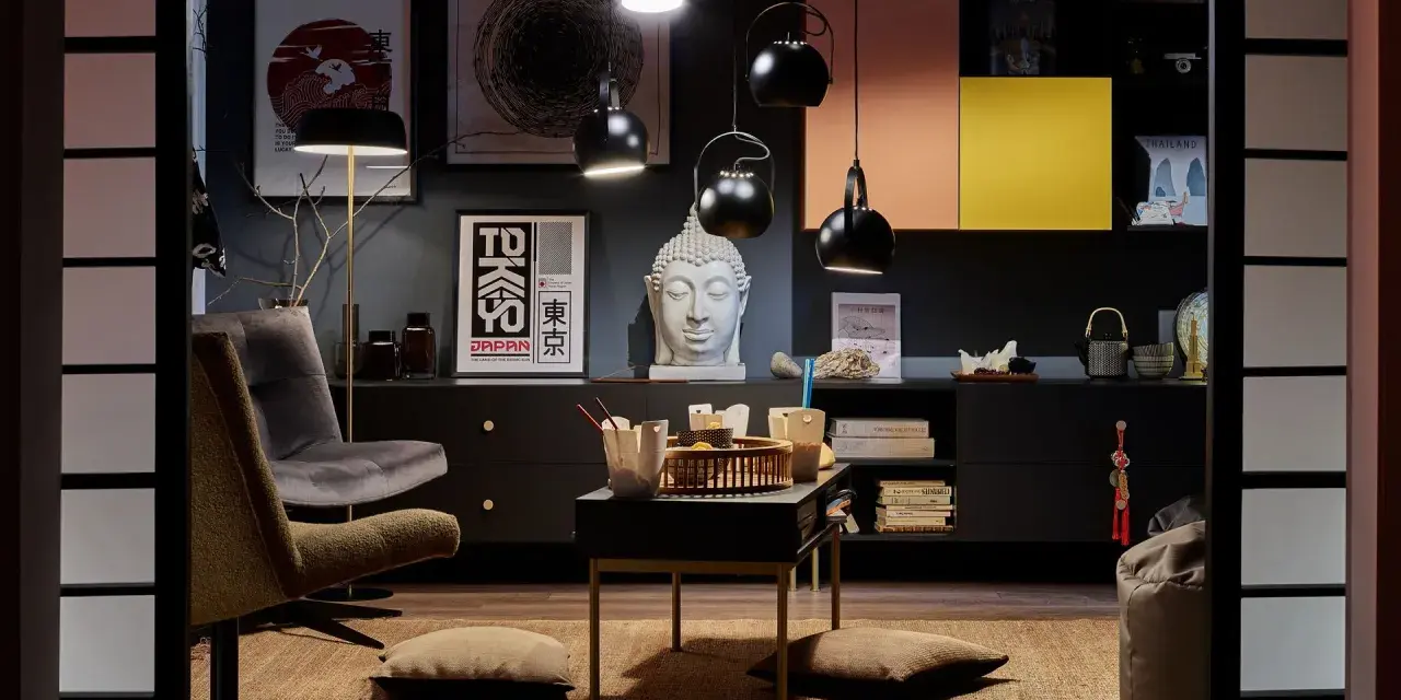 Salon w stylu eklektycznym z motywami azjatyckimi. Wygodne fotele, stolik z poduszkami, rzeźba Buddy i grafiki z Japonii tworzą przytulną atmosferę.