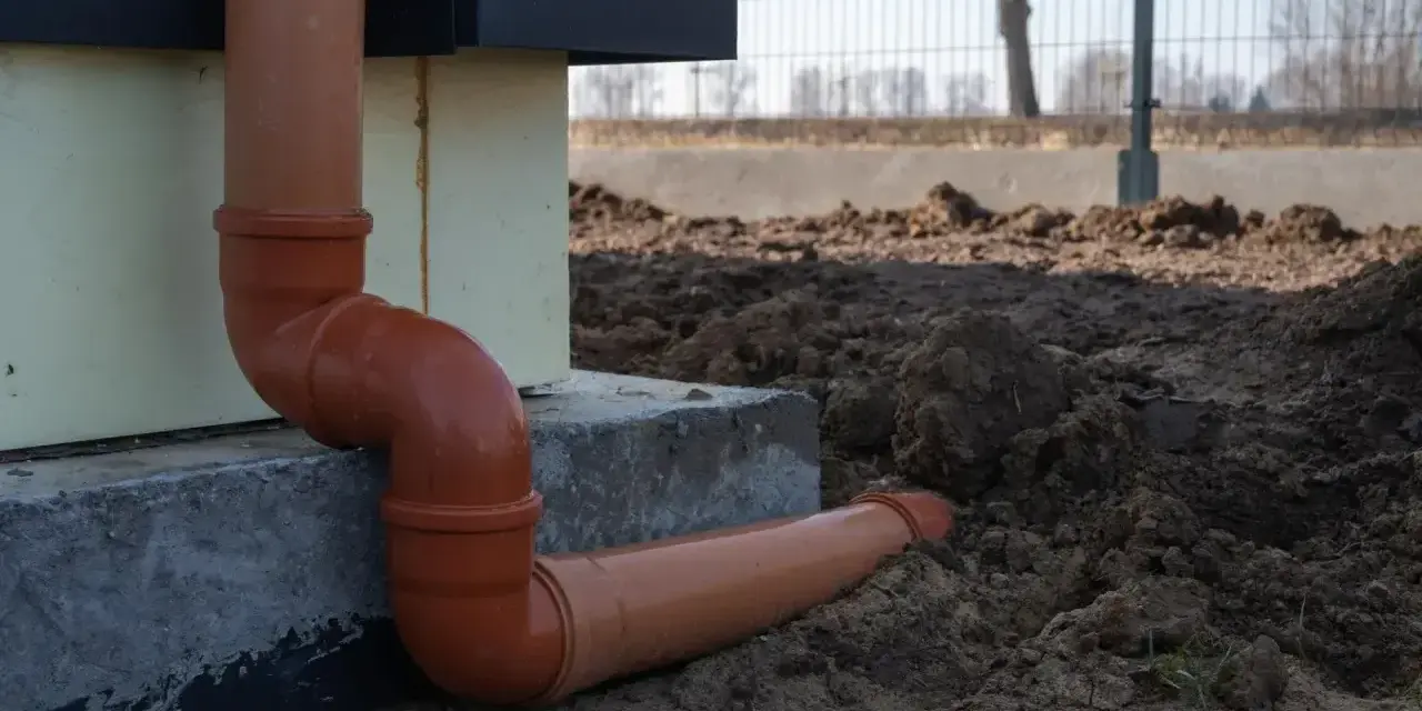 Pomarańczowe rury do odprowadzenia wody z rynien, prowadzące od budynku wprost do ziemi.