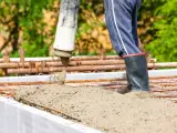 Beton B30 wylewany z pompy na zbrojenie. Pracownik w gumowcach stoi w świeżej masie, pilnując prawidłowych proporcji.