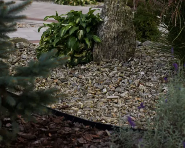 Kamień ozdobny, otoczony korą i zielenią, tworzy naturalną kompozycję w ogrodzie.