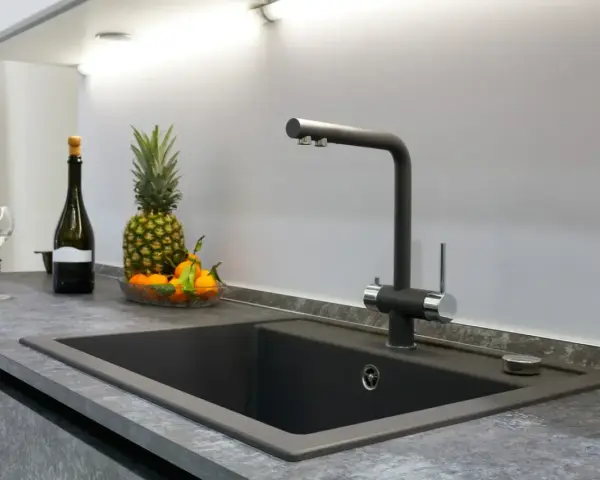 Nowoczesny zlew z baterią, obok ananas, mandarynki i butelka wina. Blat z HPL, co to jest? To trwały materiał.