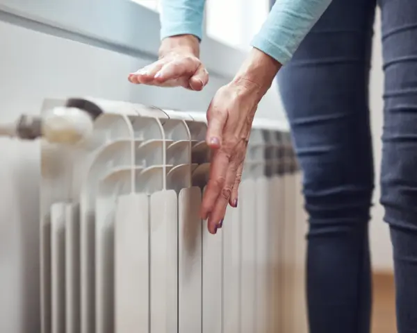 Dłonie sprawdzają temperaturę grzejnika, zastanawiając się, dlaczego grzejnik jest zimny na dole.