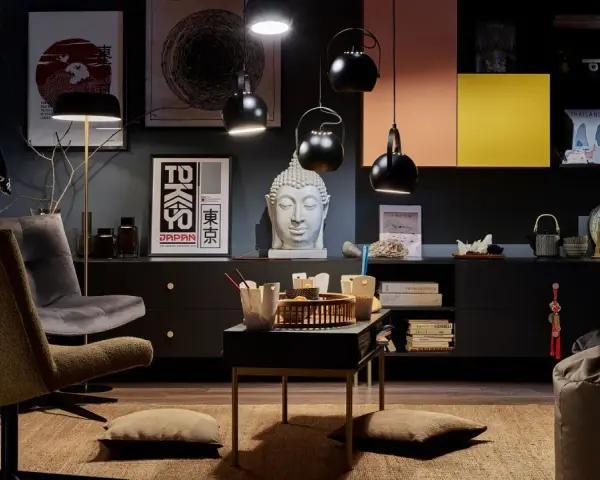 Salon w stylu eklektycznym z motywami azjatyckimi. Wygodne fotele, stolik z poduszkami, rzeźba Buddy i grafiki z Japonii tworzą przytulną atmosferę.
