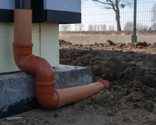 Pomarańczowe rury do odprowadzenia wody z rynien, prowadzące od budynku wprost do ziemi.