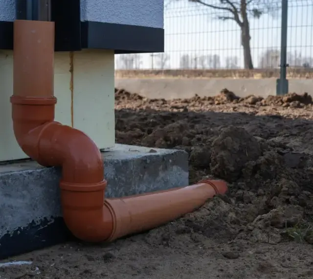 Pomarańczowe rury do odprowadzenia wody z rynien, prowadzące od budynku wprost do ziemi.