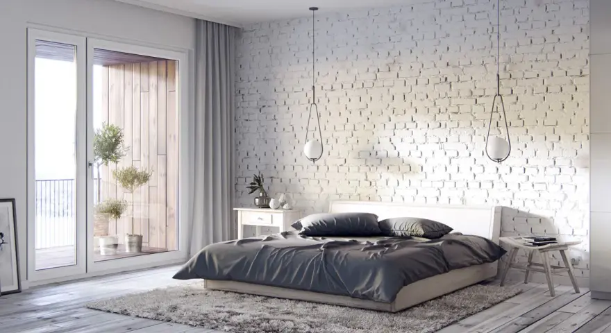 Przytulna sypialnia inspiracje: biała cegła, duże okno z widokiem na balkon, drewniana podłoga i miękki dywan tworzą relaksującą atmosferę.