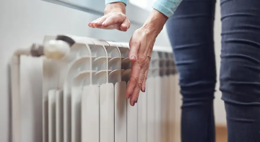 Dłonie sprawdzają temperaturę grzejnika, zastanawiając się, dlaczego grzejnik jest zimny na dole.