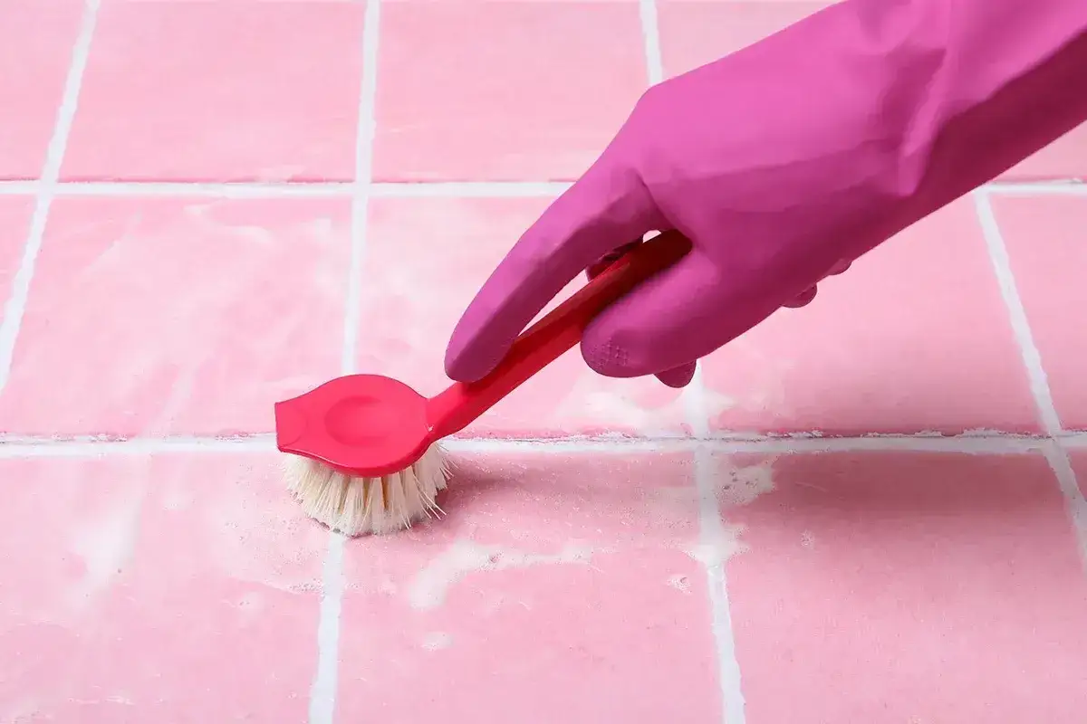 Różowa rękawica i szczotka czyszczą fugi. Dowiedz się, czym zmyć silikon, by łazienka lśniła czystością.