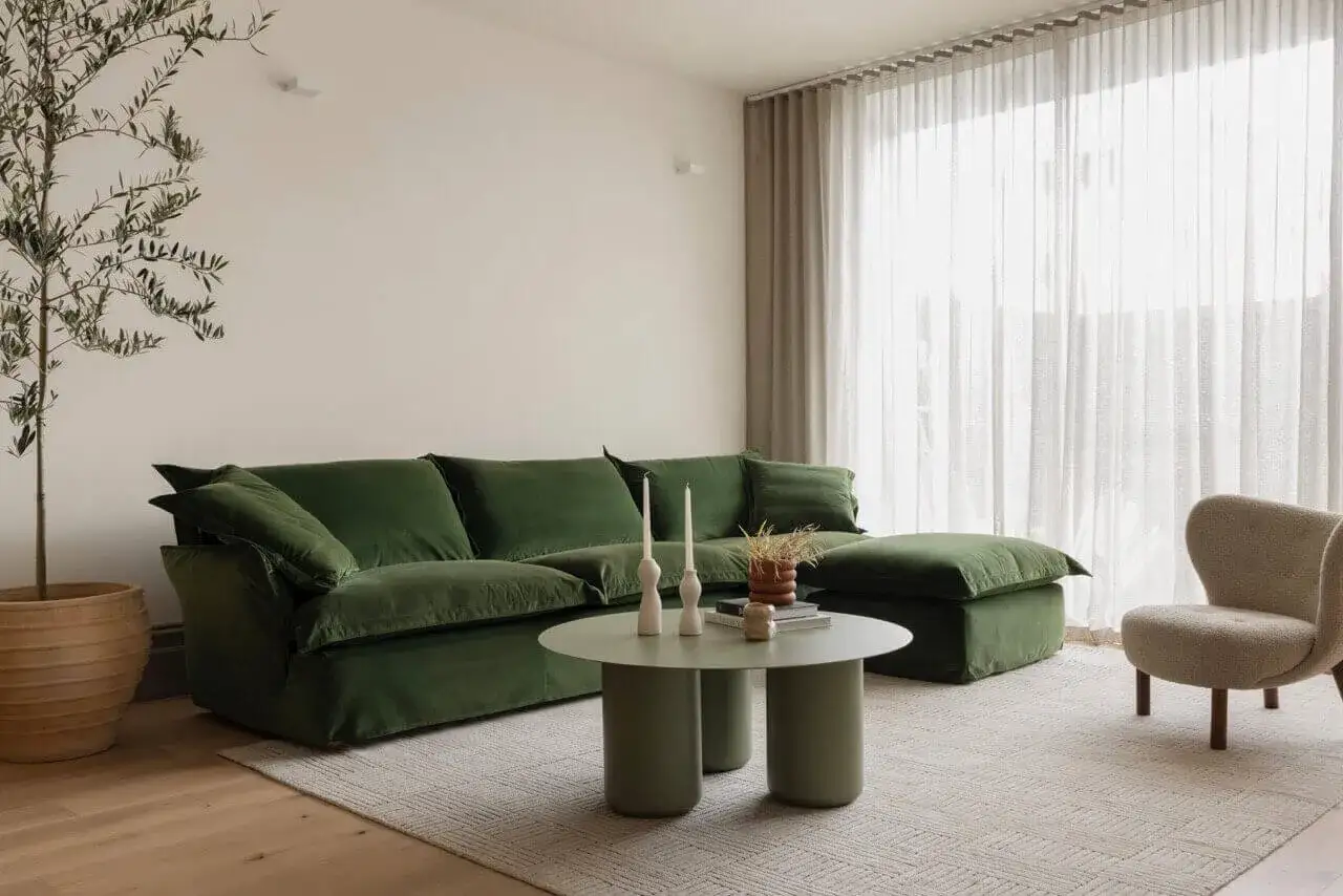 Nowoczesny salon z zieloną, aksamitną sofą i stolikiem kawowym. Oliwkowy kolor ścian tworzy przytulną atmosferę.